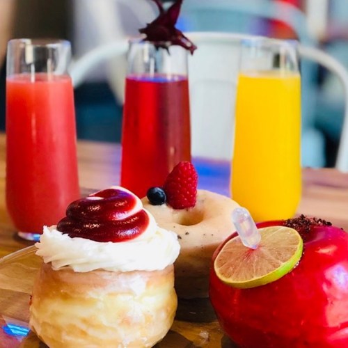 A colorful assortment of drinks and desserts, including a donut topped with cream and fruit, on a wooden table.