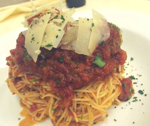 A plate of spaghetti topped with meat sauce, garnished with shaved Parmesan and fresh herbs.
