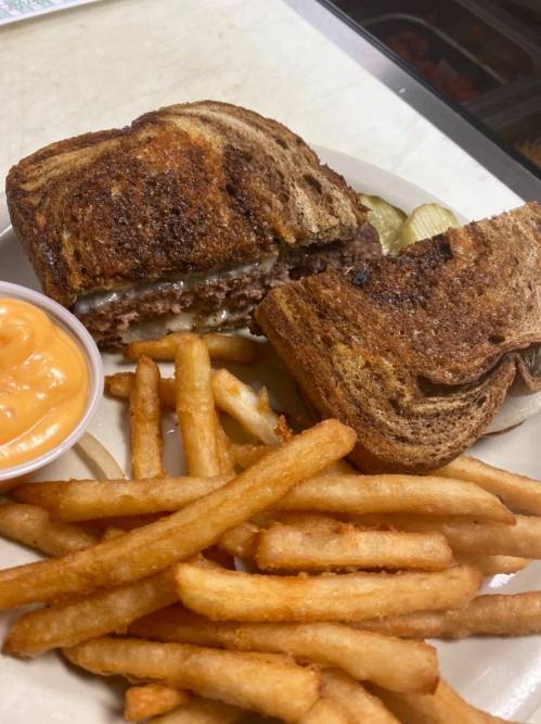 A toasted sandwich with meat and cheese, served with fries and a side of cheese sauce.