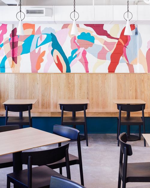 A modern café interior featuring colorful wall art, wooden seating, and minimalist black tables and chairs.