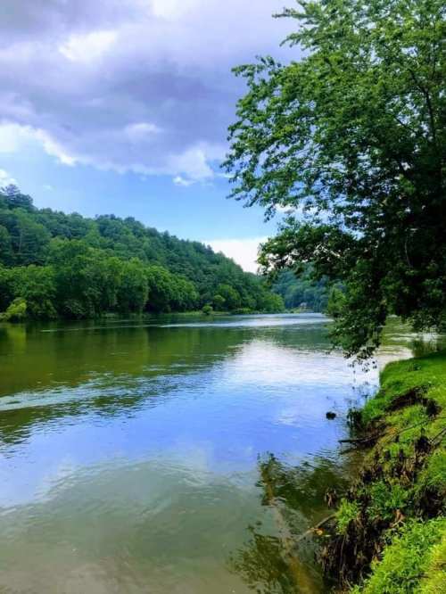 A serene river flows through lush green hills under a partly cloudy sky.