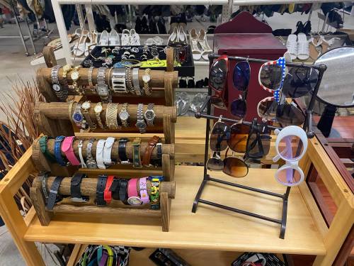 Display of various watches and sunglasses on wooden racks in a retail setting.