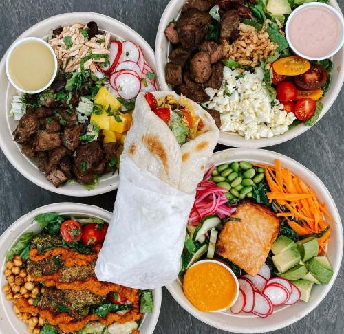 A variety of colorful bowls with meats, vegetables, and a wrapped burrito on a table.