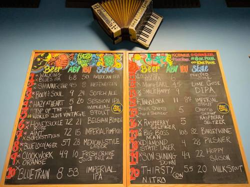 Two chalkboards displaying a beer menu with various options and prices, alongside an accordion hanging above.