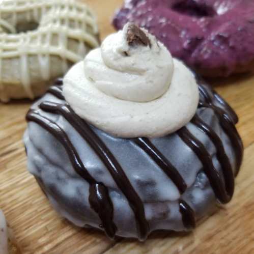 A close-up of a chocolate frosted donut topped with cream and drizzled with chocolate sauce.