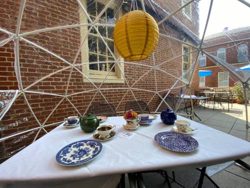 A cozy outdoor dining setup with a table set for tea, featuring various teapots and plates under a yellow lantern.
