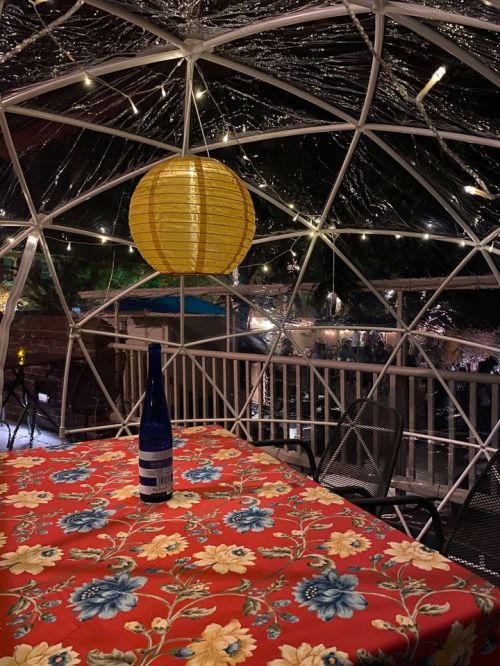 A cozy outdoor dining space with a floral tablecloth, a blue bottle, and a yellow lantern inside a clear dome.