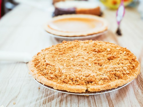 A freshly baked pie with a crumbly topping sits on a wooden table, with another pie in the background.