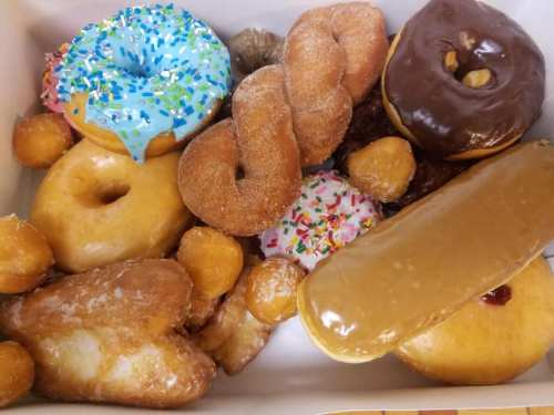 A variety of colorful donuts, including glazed, chocolate, and sprinkled, arranged in a white box.