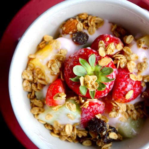 A bowl of yogurt topped with fresh strawberries, mixed fruits, nuts, and granola.