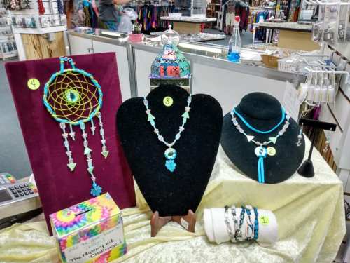 Display of colorful handmade jewelry, including a dreamcatcher, necklaces, and bracelets on a table with a soft cloth.