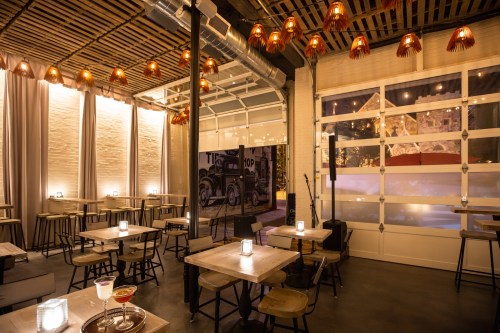 A modern restaurant interior with wooden tables, warm lighting, and a stage area, creating a cozy atmosphere.