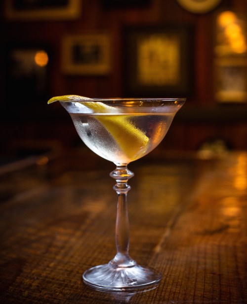 A chilled cocktail in a elegant glass, garnished with a lemon twist, set against a warm, dimly lit background.