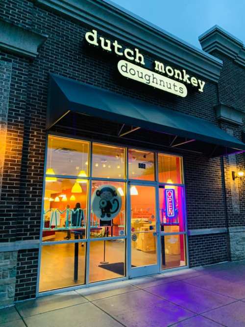 Exterior of Dutch Monkey Doughnuts shop, featuring a bright sign, open neon light, and colorful interior visible through the windows.