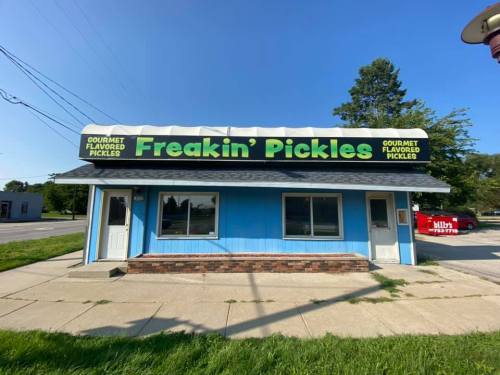 Exterior of a blue building with a sign that reads "Freakin' Pickles" offering gourmet flavored pickles.
