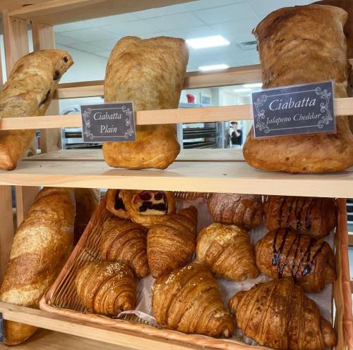 A display of fresh ciabatta loaves and croissants on wooden shelves, labeled with their flavors.