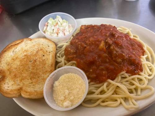 A plate of spaghetti topped with meat sauce, served with a side of coleslaw, grated cheese, and toasted bread.