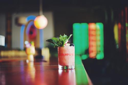 A vibrant cocktail with mint leaves sits on a bar, surrounded by colorful lights in a lively setting.