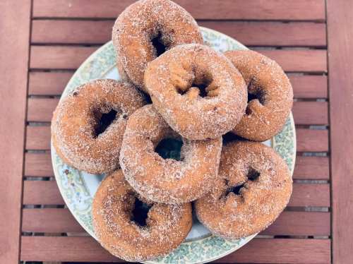 A plate of freshly made, sugar-coated donuts stacked on a wooden table.