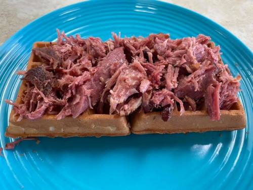 A blue plate holds two waffles topped with shredded meat, creating a savory dish.