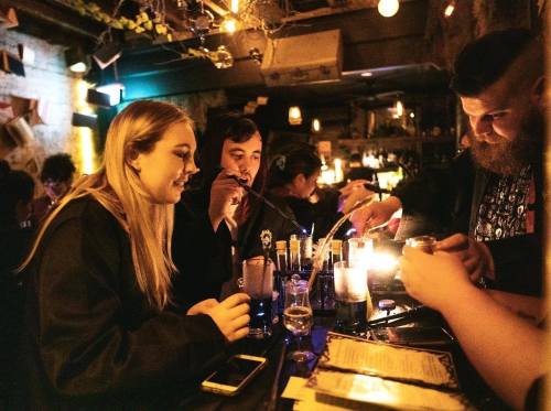 A group of friends enjoying drinks at a dimly lit bar, with candles and vibrant decor in the background.
