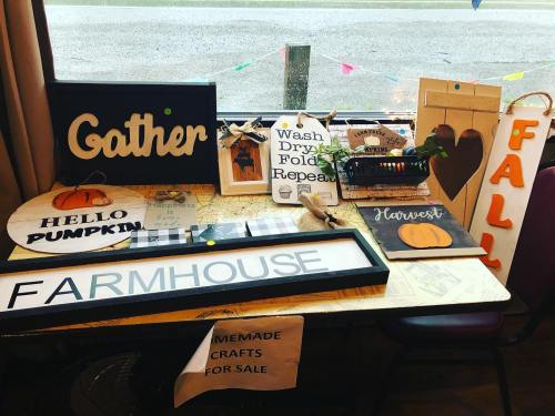A display of homemade crafts for sale, featuring signs with autumn themes like "Gather," "Hello Pumpkin," and "Farmhouse."