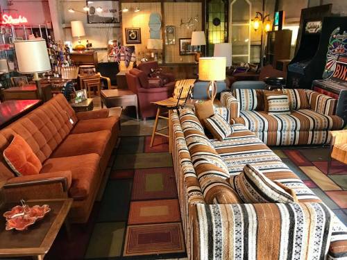 A vintage furniture store featuring colorful sofas, armchairs, and decor in a cozy, retro setting.