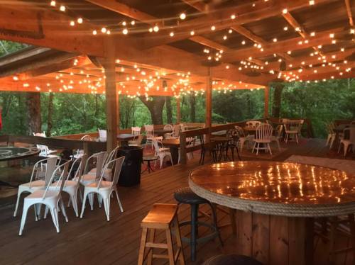 Cozy outdoor dining area with string lights, wooden tables, and chairs surrounded by greenery.