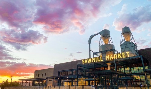 Sawmill Market building at sunset, featuring large silos and colorful clouds in the sky.