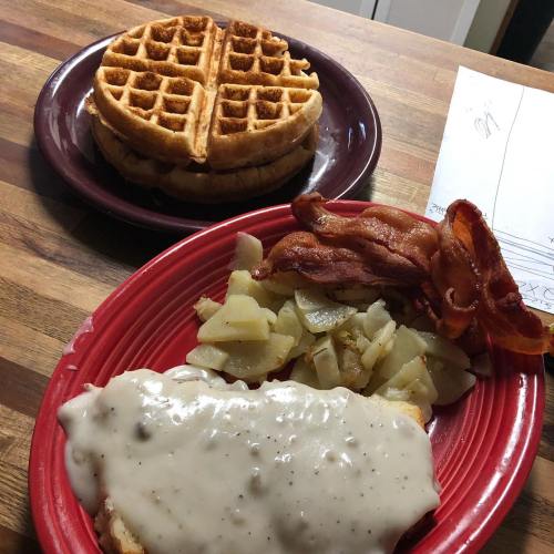 A plate with waffles, bacon, and potatoes topped with gravy, set on a wooden table.