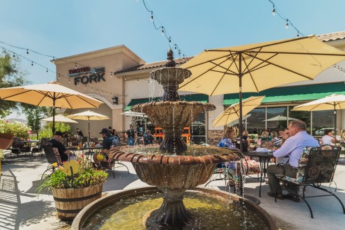 Outdoor dining area at Twisted Fork with a fountain, umbrellas, and patrons enjoying their meals in a sunny setting.