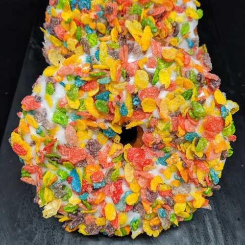 Two colorful donuts covered in white icing and topped with vibrant, crunchy cereal pieces.