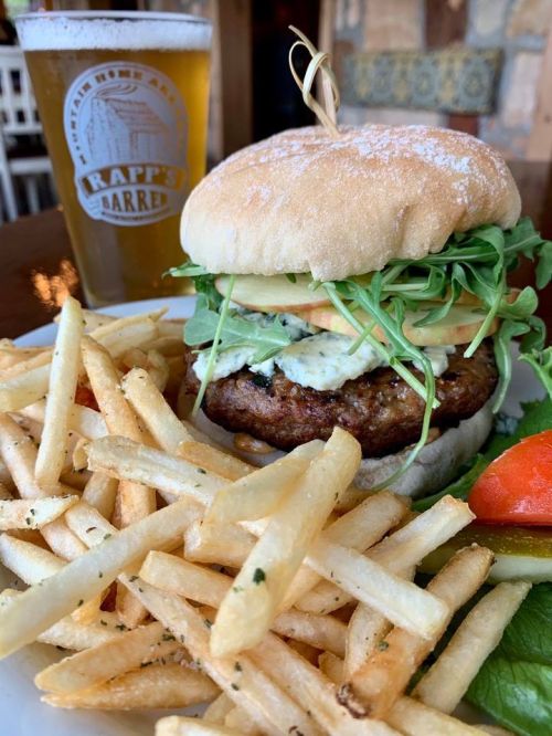 A juicy burger with lettuce, tomato, and sauce, served with crispy fries and a glass of beer in the background.