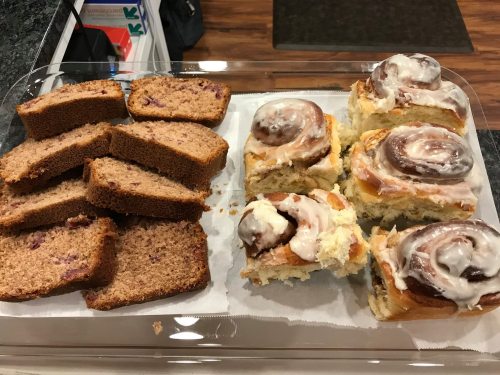 A tray with slices of purple bread and frosted cinnamon rolls, arranged neatly on parchment paper.