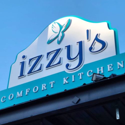 Sign for "Izzy's Comfort Kitchen" featuring a butterfly logo against a blue sky.