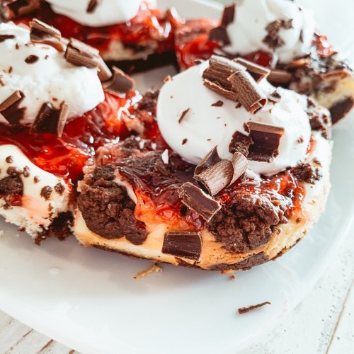 A close-up of dessert featuring a crust topped with cherry filling, whipped cream, and chocolate shavings.