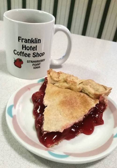 A slice of cherry pie on a plate next to a coffee mug from Franklin Hotel Coffee Shop in Strawberry Point, Iowa.