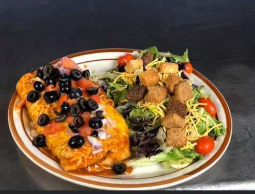 A plate featuring two enchiladas topped with cheese, olives, and a side salad with croutons and cherry tomatoes.