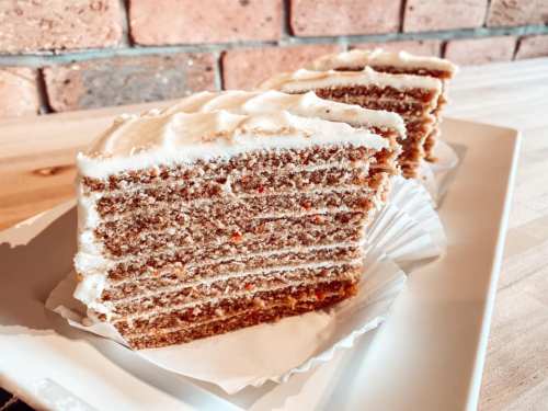 A slice of layered cake with cream frosting on a white plate, set against a brick wall background.