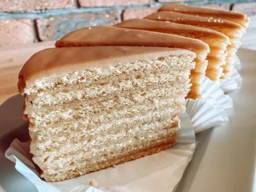 Slices of layered cake with a smooth frosting, arranged neatly on a plate against a brick background.