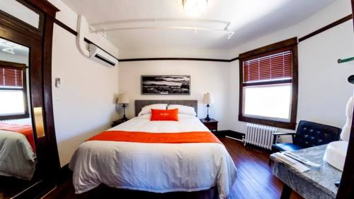 Cozy hotel room with a double bed, orange accent pillow, wooden accents, and a large mirror reflecting the space.
