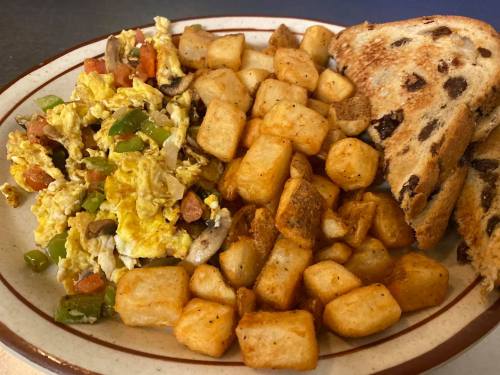 A plate of scrambled eggs with vegetables, golden-brown potatoes, and toasted bread.