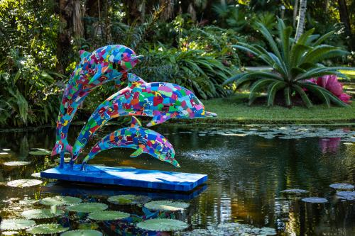 Colorful dolphin sculpture leaping over a pond surrounded by lush greenery and water lilies.