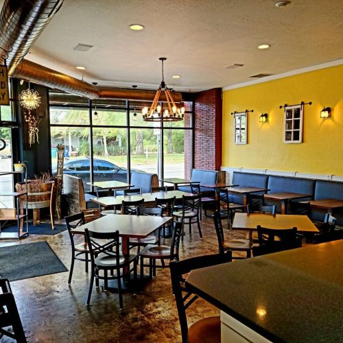 Bright café interior with tables, chairs, and large windows, featuring yellow walls and a cozy atmosphere.
