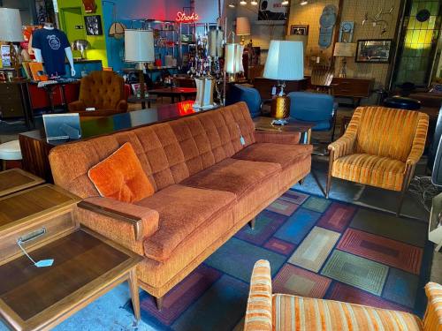 A retro furniture store featuring an orange sofa, striped chairs, and various vintage decor items.