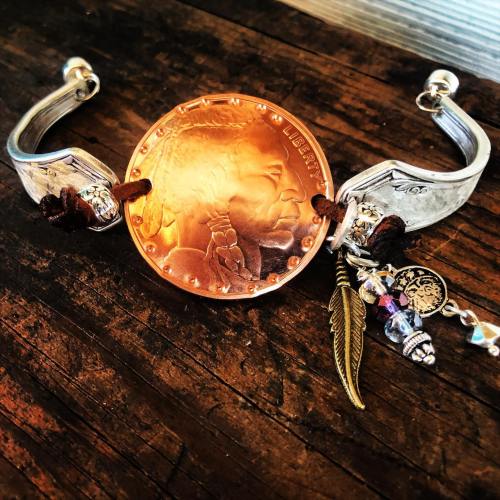 A unique bracelet featuring a large copper coin, silver accents, and decorative charms on a wooden surface.