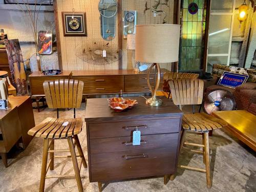 A vintage furniture display featuring a wooden table, two chairs, a lamp, and decorative items in a cozy setting.