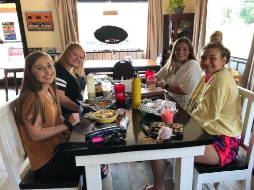 Four friends sitting at a table in a restaurant, enjoying food and drinks, smiling at the camera.