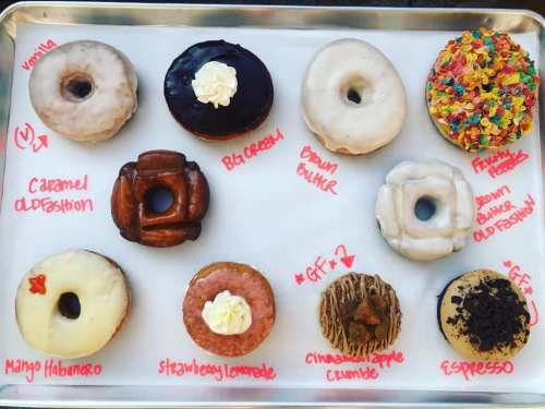 A tray of assorted donuts labeled with flavors: vanilla, caramel old-fashioned, blueberry, brown butter, and more.