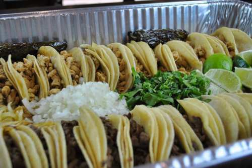 A tray of assorted tacos with chicken, beef, onions, cilantro, lime, and green chiles arranged neatly.
